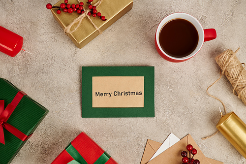 Merry Christmas greeting card near decorated gift boxes and mug of hot chocolate on textured surface