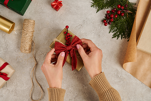 cropped view of woman decorating gift box with red bow near craft supplies, Christmas backdrop