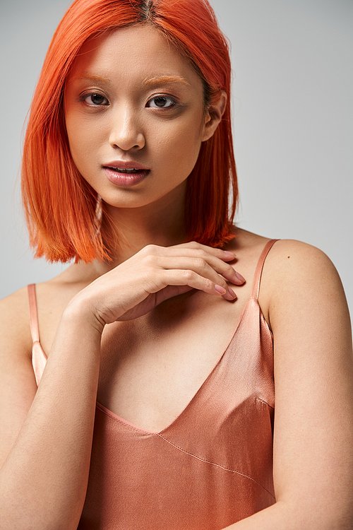 attractive asian woman in silk slip dress standing and looking at camera on grey backdrop, elegance