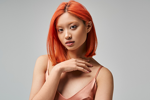 portrait of charming young asian woman in silk slip dress looking at camera on grey background