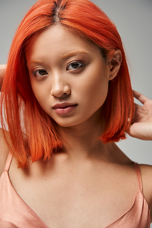 portrait of young asian woman with red hair looking at camera on grey background, natural beauty