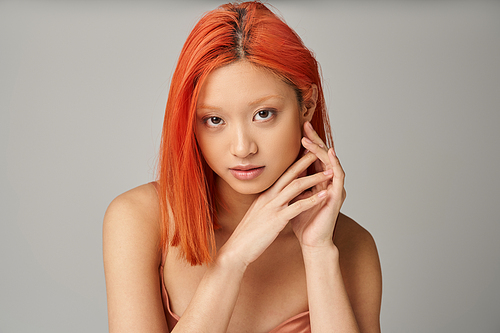 portrait of charming young asian woman with perfect skin looking at camera on grey background