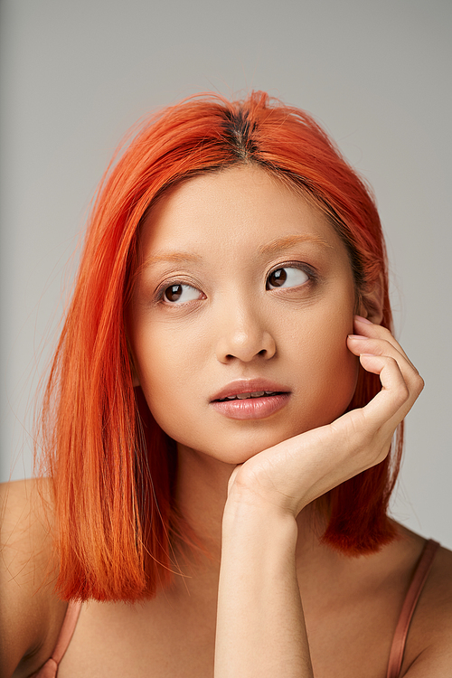 portrait of attractive and young asian woman with perfect skin  daydreaming on grey backdrop