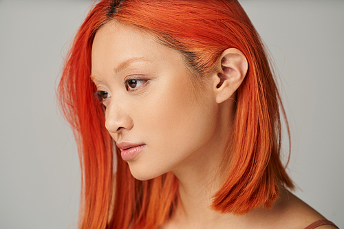 portrait of delicate young asian woman with perfect skin and red hair posing on grey background