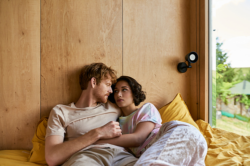 interracial couple having tender moment while lying together on bed and looking at each other