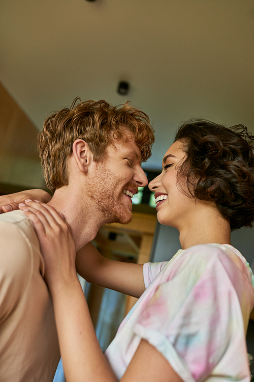 side view of happy interracial couple looking at each other and laughing, having a good time