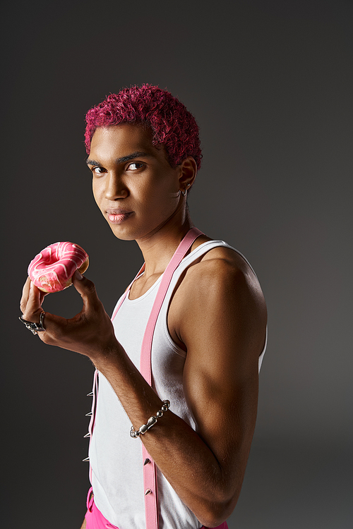 jolly pink haired man in stylish attire with pink hair posing with donut in hands, fashion and style