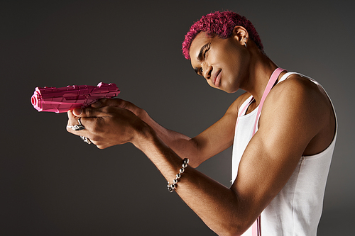 pink haired african american male model in pants with suspenders aiming his pink toy gun aside