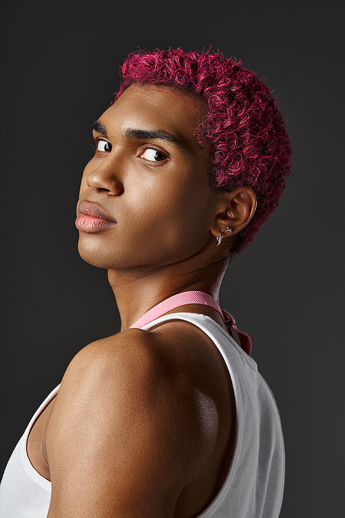 portrait of handsome young man with pink hair looking at camera on gray backdrop, fashion concept