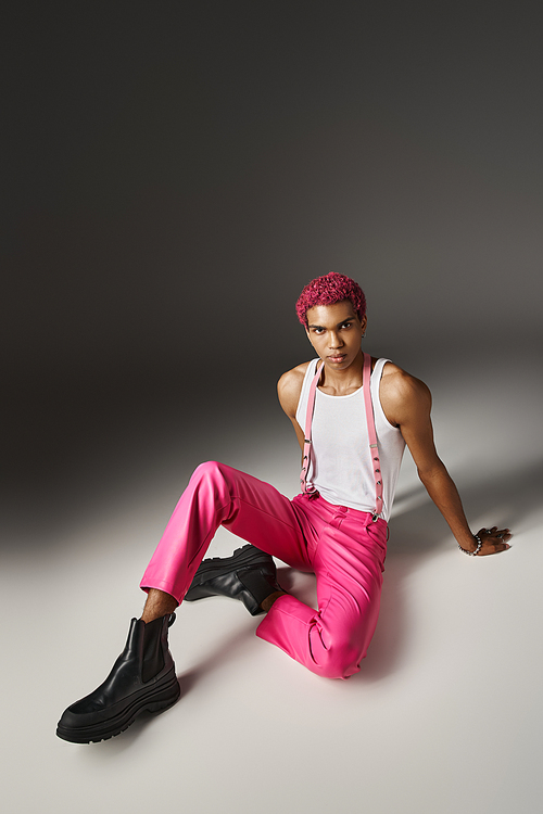 stylish pink haired man in pink vibrant outfit with black boots sitting on floor, fashion concept