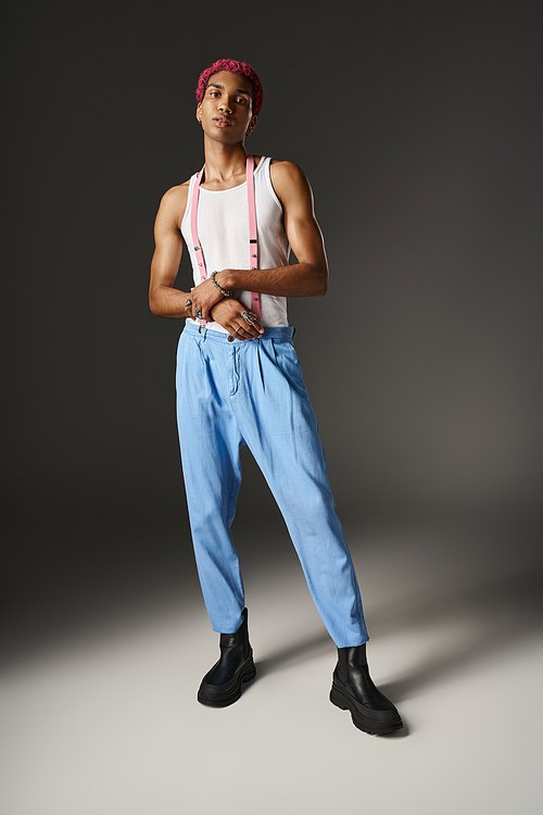 stylish african american man n blue pants with pink suspenders looking at camera, fashion concept