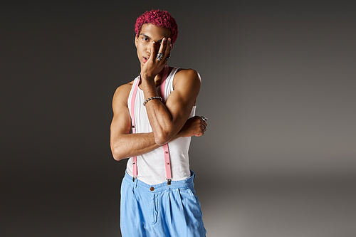 voguish pink haired man posing with slightly crossed arms on gray backdrop, fashion concept