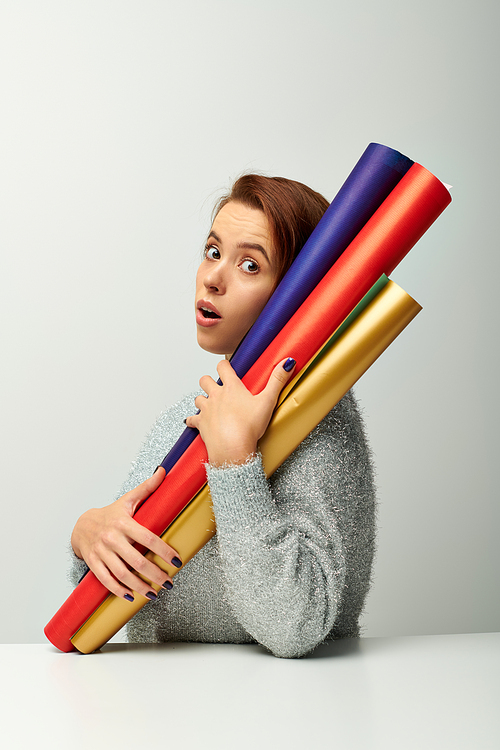 surprised woman with short hair holding colorful wrapping paper on grey backdrop, Christmas concept