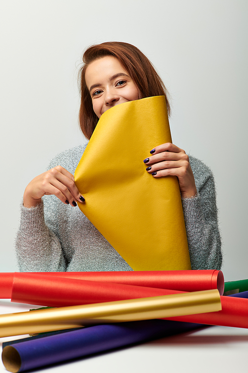 season of joy, young woman in sweater holding yellow Christmas gift paper on grey backdrop