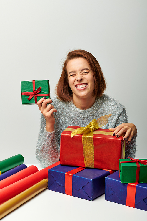 happy woman in winter sweater near wrapped Christmas present and colorful gift paper on grey
