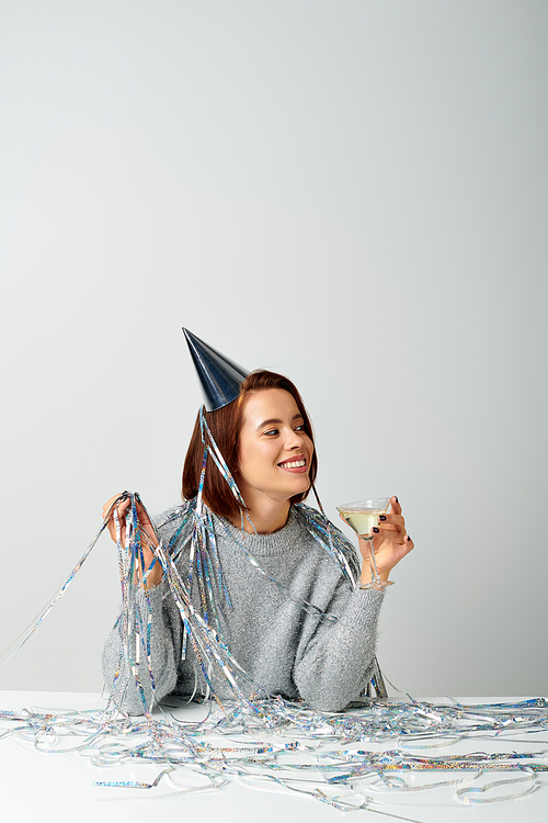 happy woman in party cap with tinsel on head holding glass of champagne while celebrating Christmas