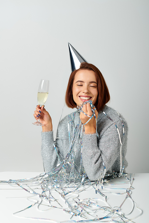 happy woman in party cap and tinsel on head holding champagne glass while making a wish on New year