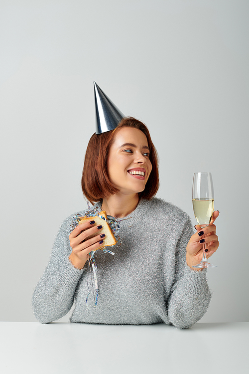 happy woman in party cap holding sandwich with tinsel and champagne glass, celebrating New year
