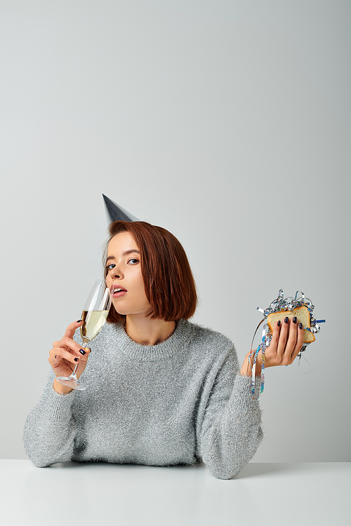 young woman in party cap drinking champagne and holding sandwich with tinsel, Merry Christmas