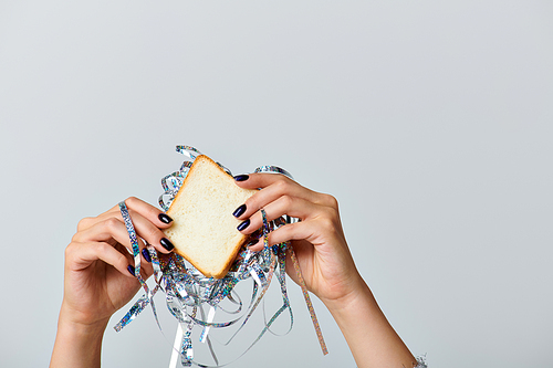 partial view of woman holding sandwich with tinsel on grey backdrop, Happy New Year concept