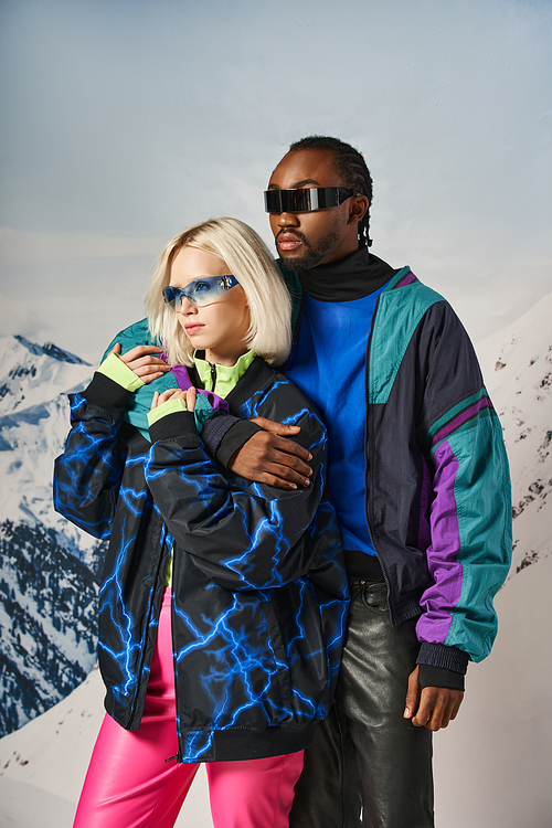 beautiful multiracial couple in vibrant bold outfits and stylish sunglasses hugging warmly, winter