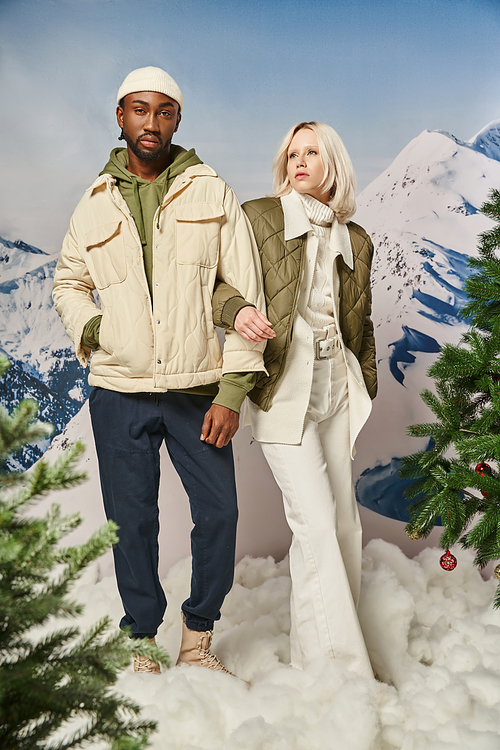 beautiful multicultural couple in warm stylish clothes posing with hand on arm, winter concept