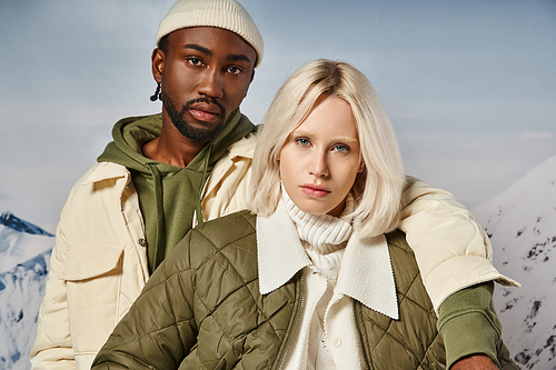 portrait of voguish multiracial couple in warm vibrant attire looking at camera, winter concept