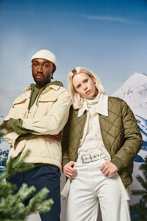 attractive couple in warm winter jackets posing together on snowy backdrop, winter fashion
