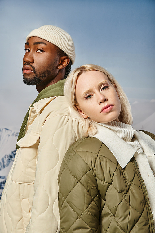 portrait of fashionable couple in warm attire posing back to back looking at camera, winter fashion