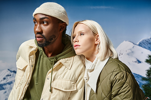 attractive multiracial couple in winter jackets posing together and looking away, style and fashion