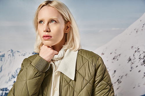 beautiful blonde woman in khaki jacket posing with her hand on chin and looking away, winter fashion