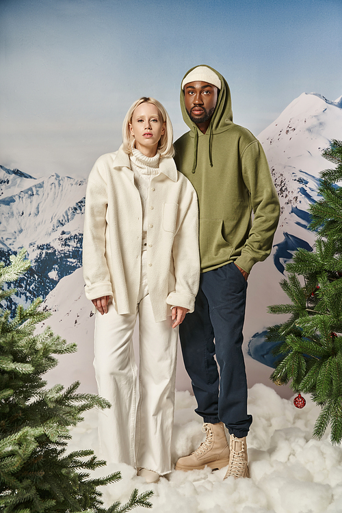 beautiful multicultural couple standing side by side with mountain background, winter fashion
