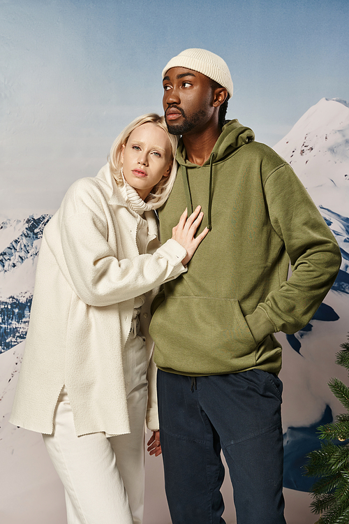 young blonde woman with her hand on her boyfriend chest with snowy backdrop, winter fashion