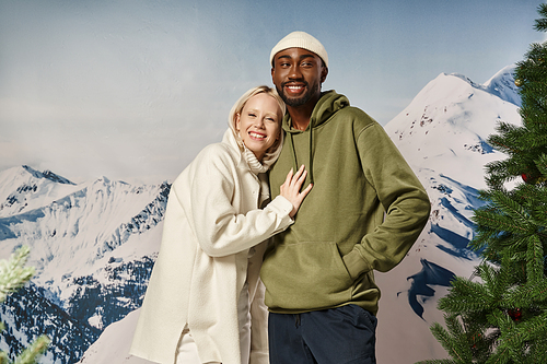 happy blonde woman hugging with african american boyfriend with mountain backdrop, winter fashion