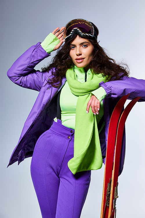 winter activity, attractive woman with curly hair posing in active wear with puffer jacket and skis