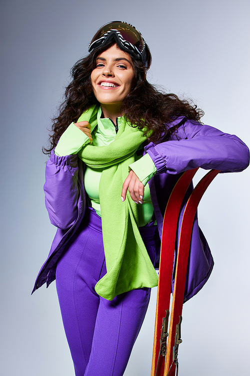 winter activity, smiling woman with curly hair posing in active wear with puffer jacket and skis