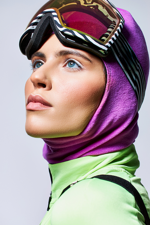 portrait of woman in ski clothes with balaclava looking up on grey, female model with blue eyes