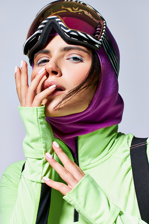 portrait of woman in ski clothes with balaclava posing on grey backdrop, model with blue eyes