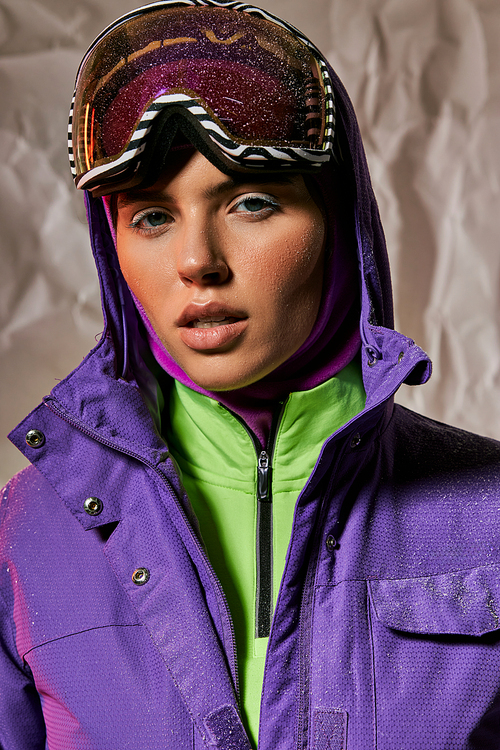 crisp air, beautiful woman in balaclava and ski googles posing in purple winter jacket on grey