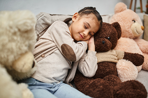 adorable elementary age girl sleeping among soft teddy bears on couch in modern living room