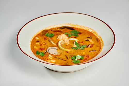 tasty Thai soup with coconut milk, shrimp, lemongrass and cilantro on grey backdrop, Tom yum