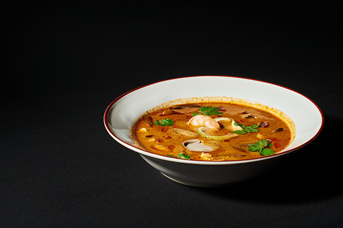 spicy Tom yum soup with coconut milk, shrimp, lemongrass and cilantro on black background. close up