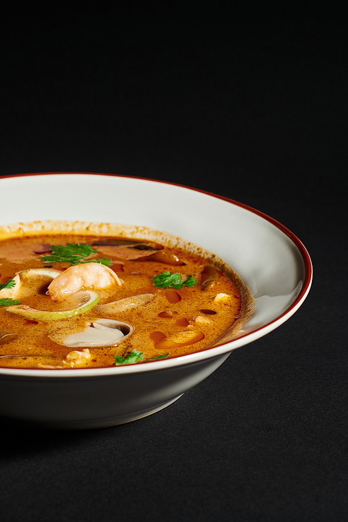 spicy Tom yum soup with coconut milk, shrimp, lemongrass and cilantro on black background, close up