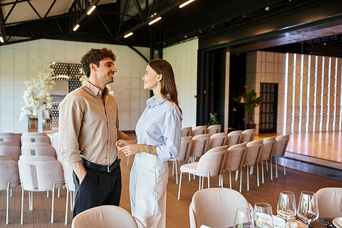 smiling couple talking near festive table with banquet setting in event hall with wedding decor