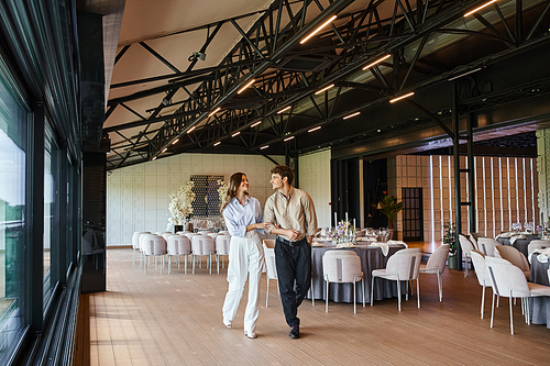 happy couple in love walking along banquet hall with wedding decor and festive tables, special day