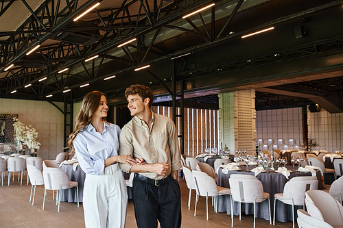 happy romantic couple smiling at each other in modern banquet hall with decorated festive tables