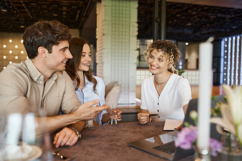 smiling man talking to event manager near happy girlfriend in banquet hall, wedding preparation