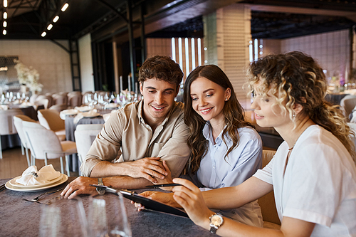 wedding organizer showing contract to smiling couple while sitting at festive table in event hall