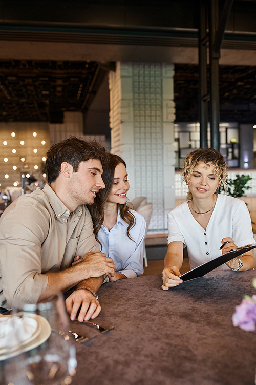 banquet coordinator showing contract to happy couple while sitting at festive table in event hall