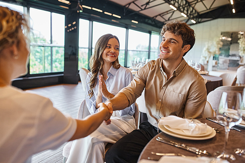 smiling man shaking hands with event manager near overjoyed girlfriend in modern wedding venue